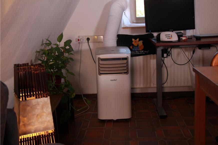 Eine mobile Klimaanlage ist per Abluftschlauch an eine Fensterabdichtung angeschlossen.